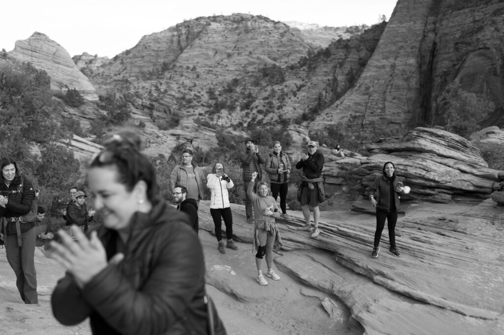 A crowd of people cheers on the couple at the end of a hike at Zion National Park