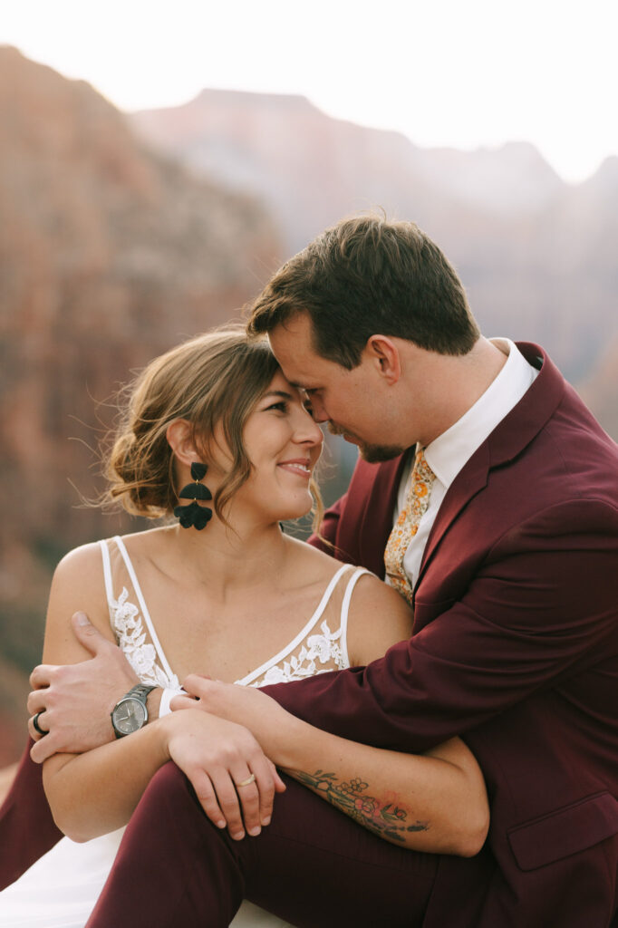 the couple touches foreheads while sitting on a cliff in Zion National Park