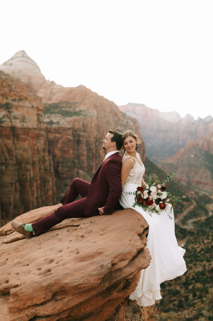 The couple sit back to back on the side of a cliff in Zion National Park
