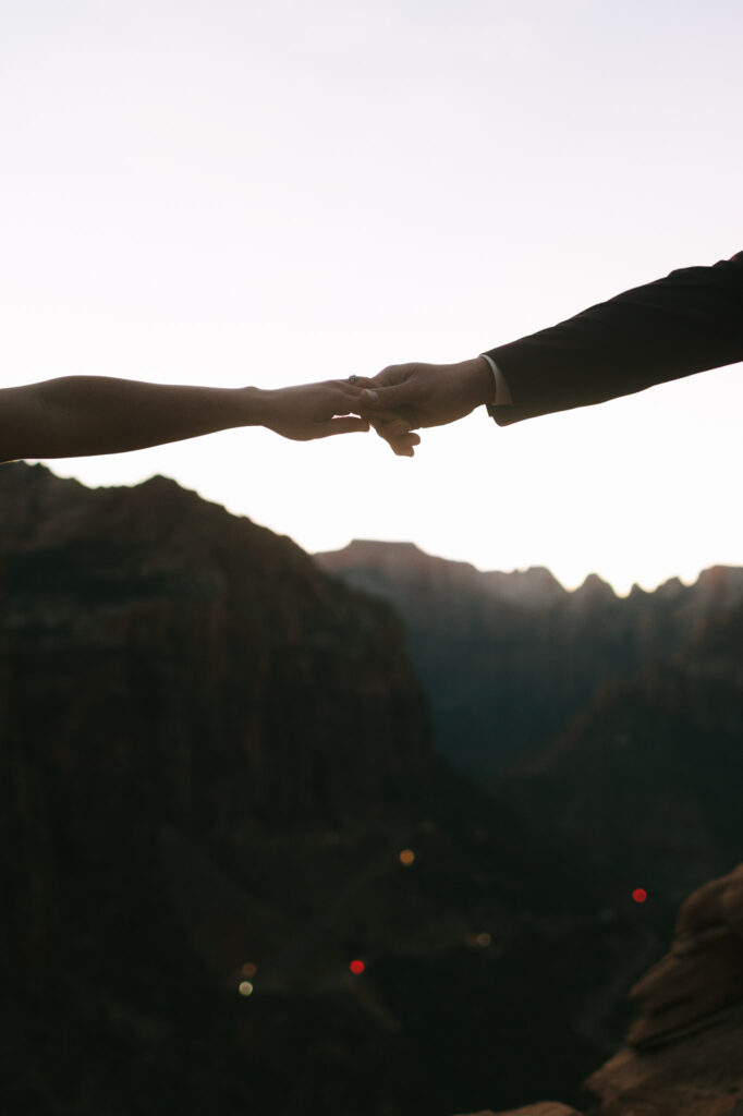 The couple holds hands on the side of a cliff in Zion National Park 
