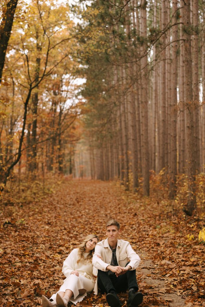 Sophia and Brad sit in the leaves for their engagement photos