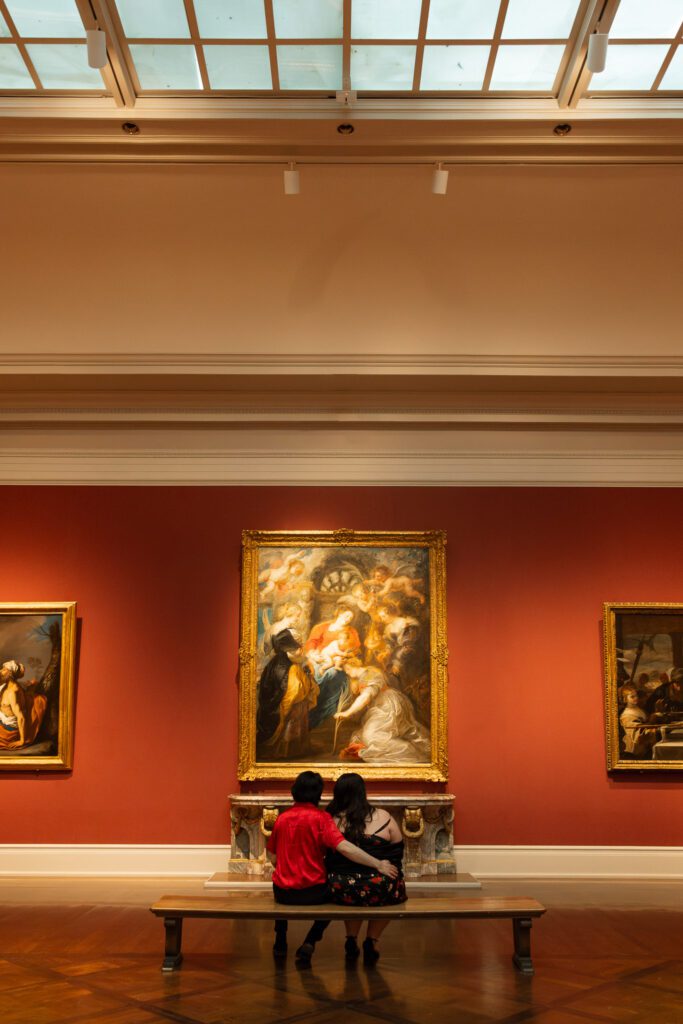 Adam and Bethany sit on a bench in the grand gallery of the art museum