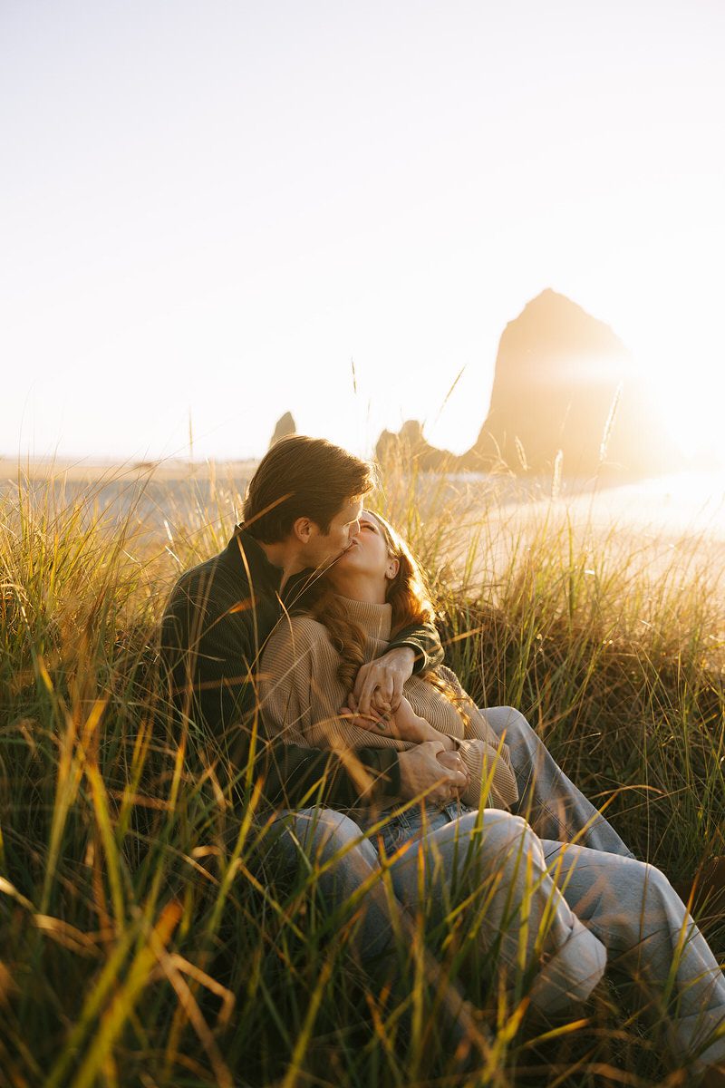 J&L hug and kiss while sitting on a dune