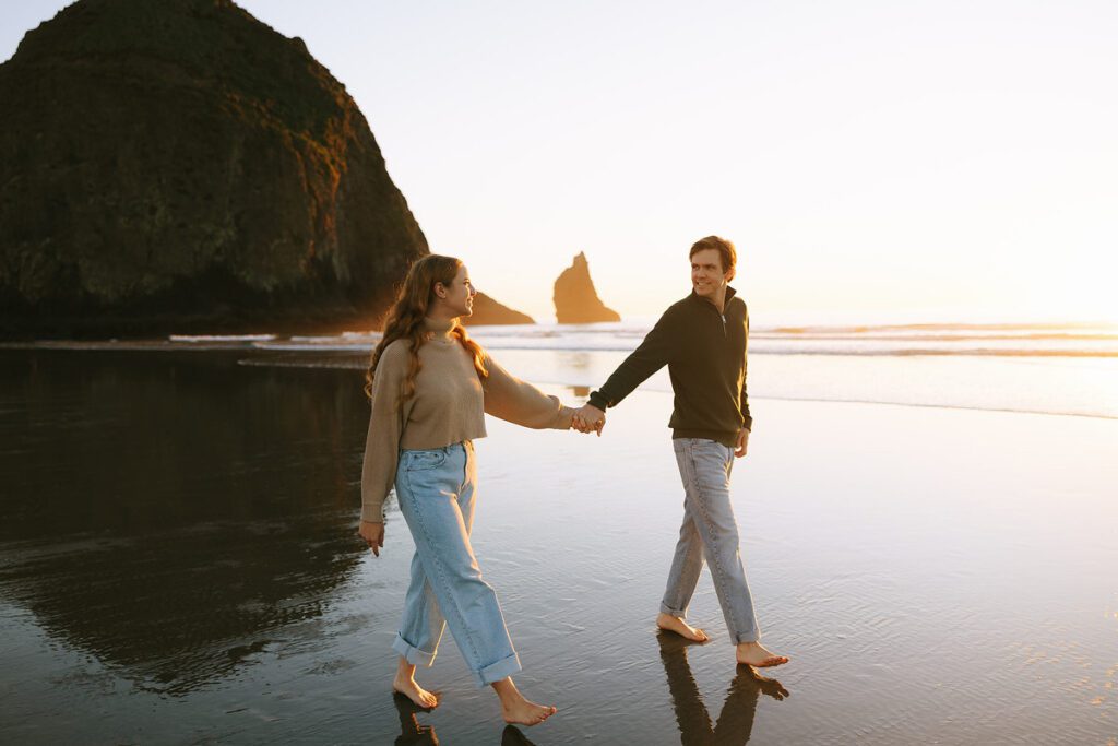 Jason and Leah walk down the shore of the Oregon coast, away from Haystack rock