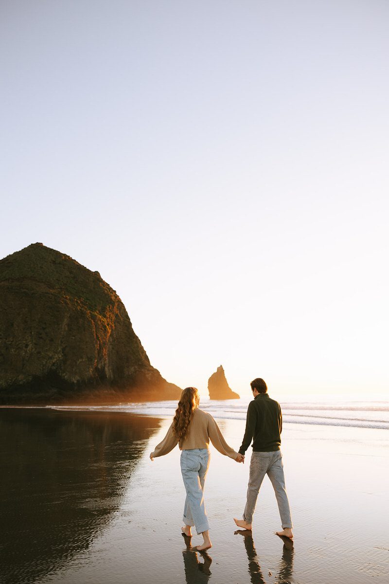 Jason and Leah walk down the shore of the Oregon coast, towards Haystack rock