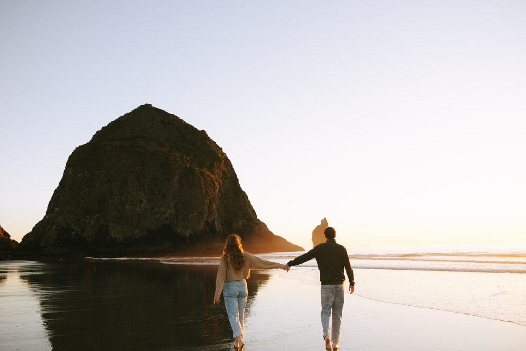 Jason and Leah walk down the shore of the Oregon coast, towards Haystack rock