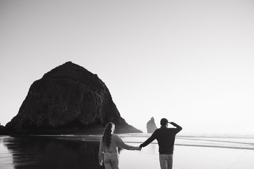 Jason and Leah walk down the shore of the Oregon coast, towards Haystack rock