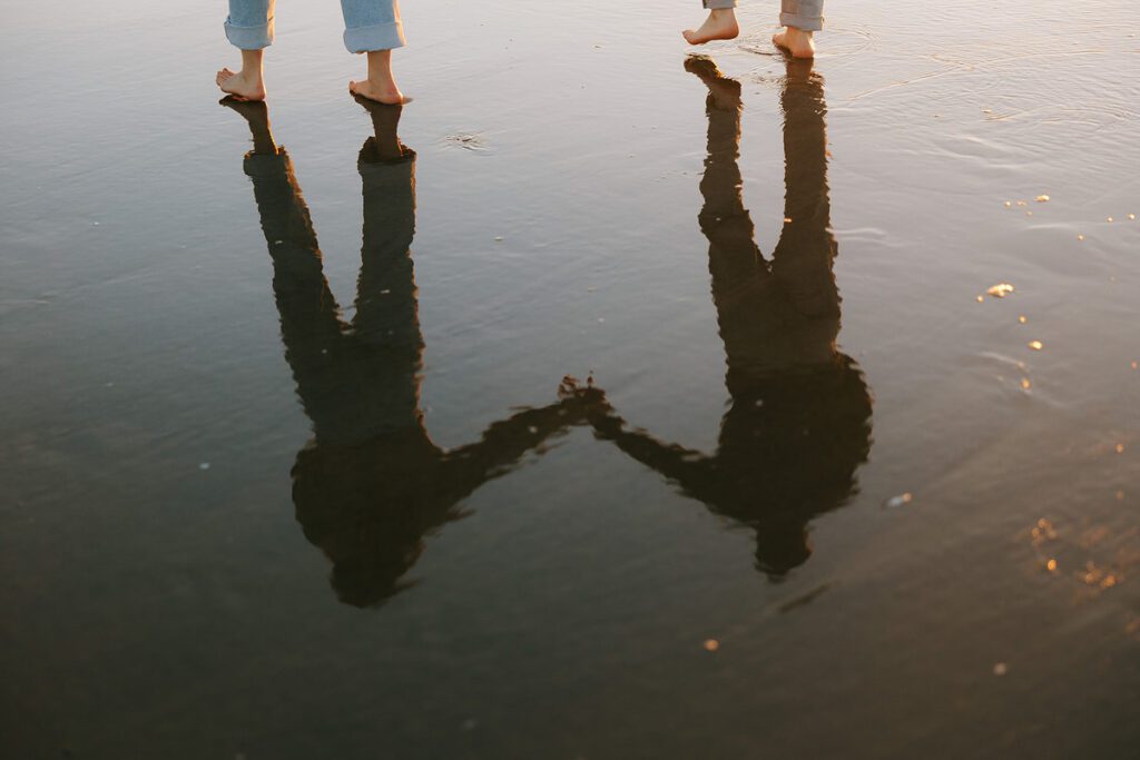 A reflection of Jason and Leah as they walk down the shore of the Oregon coast, towards Haystack rock