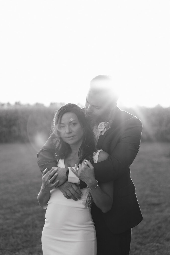 Karis looks at the camera during her wedding portraits at sunset, Tony kisses the side of her head