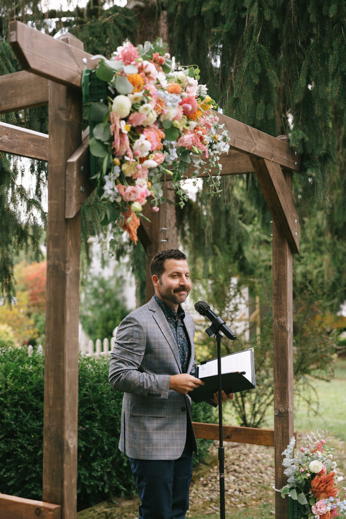 The brides brother officiates the wedding, standing beneath the wildflower arch designed by the owner of Bloom and Bower