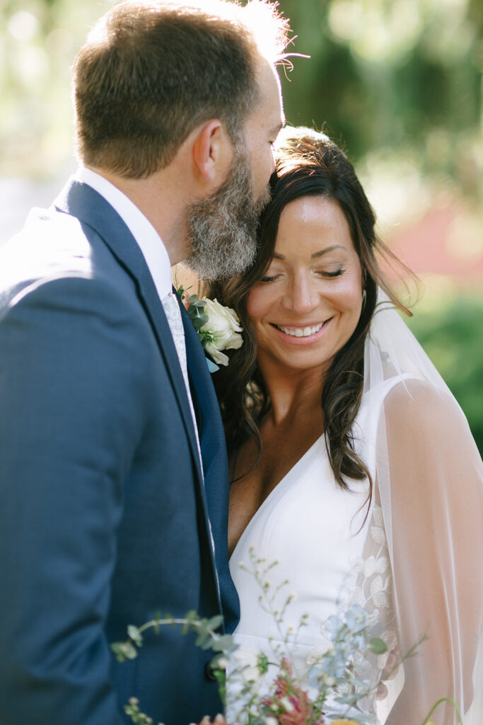 Tony kisses Karis on her temple during their portraits while she hold her bouquet