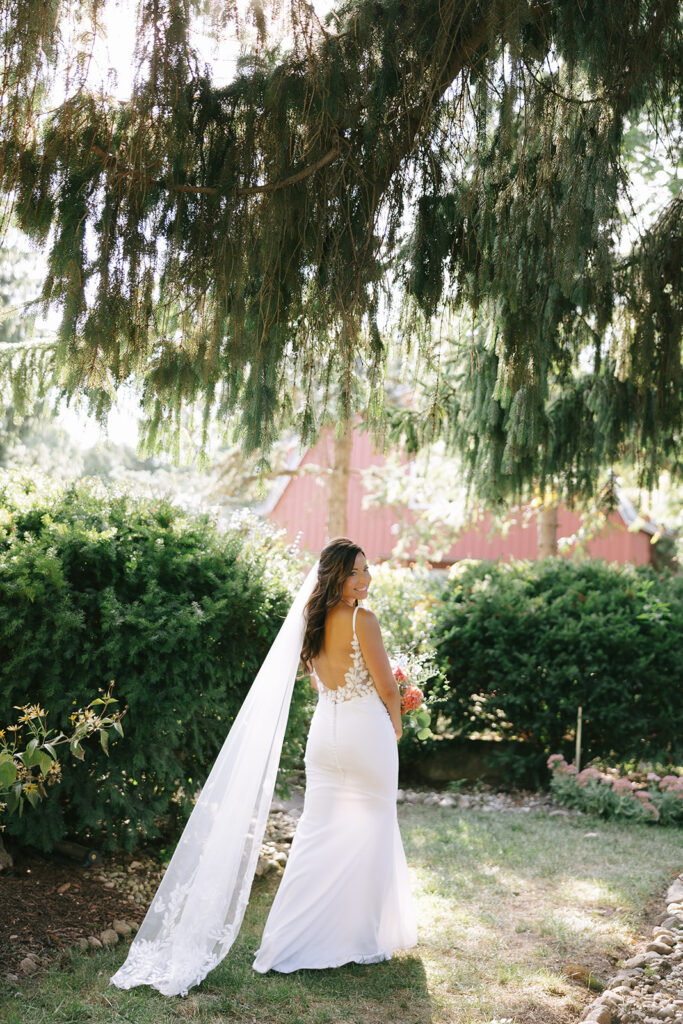 Karis walks in the garden at Bloom and Bower, holding her floral bouquet and trailing her custom veil behind her