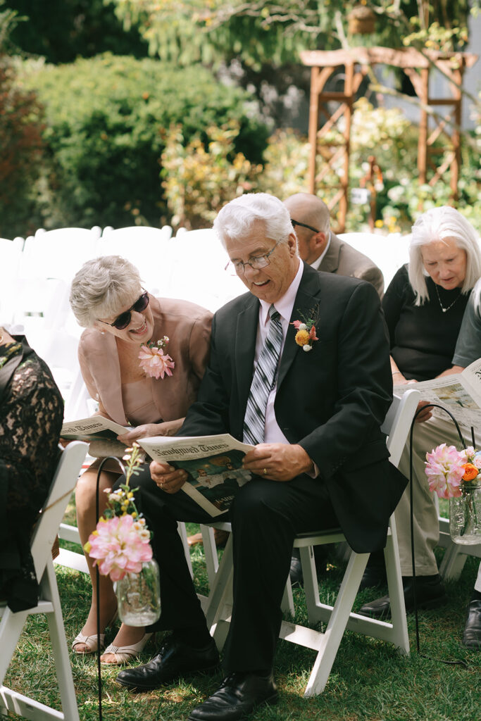 The grooms dad laughs while reading their wedding day newspaper while waiting for their ceremony to start