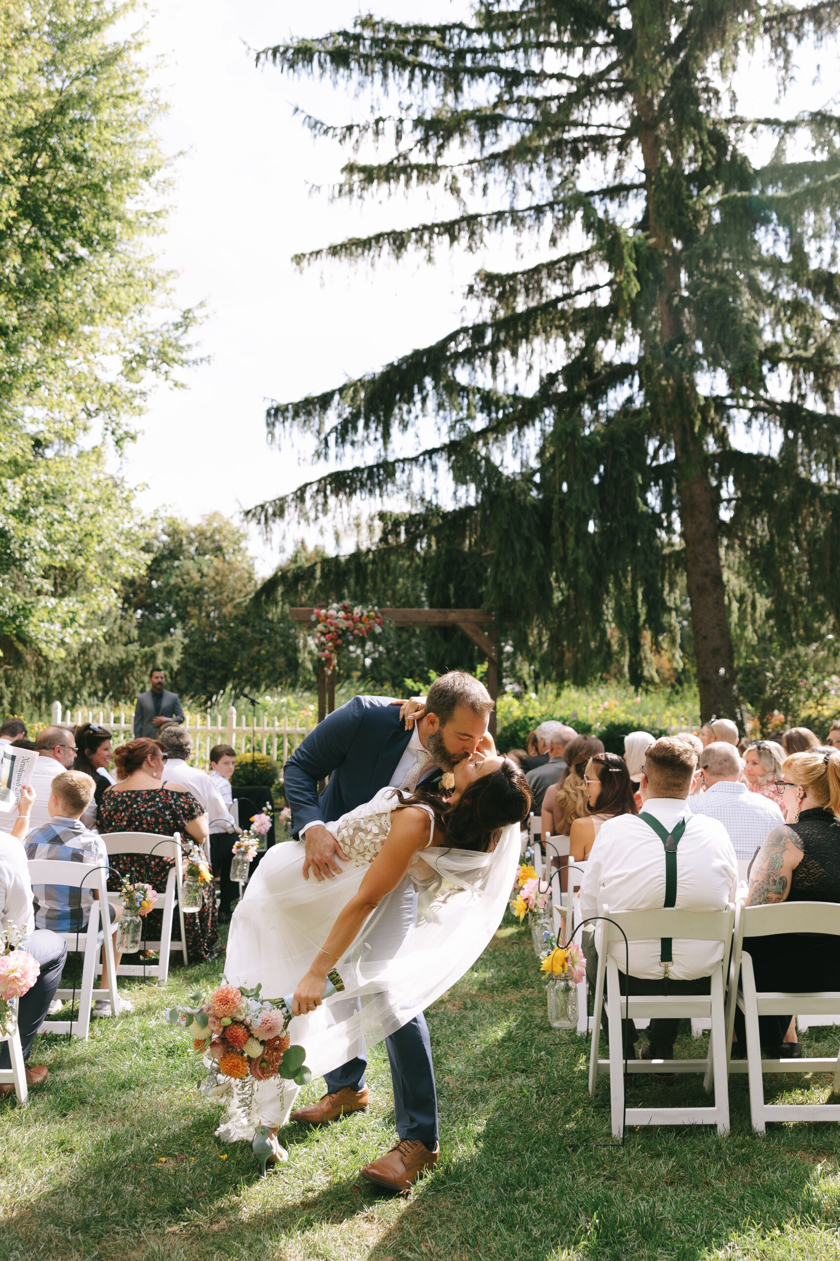 Tony dips Karis, as they walk back up the aisle during their wedding. Karis carries her wildflower bouquet and wears a custom dress