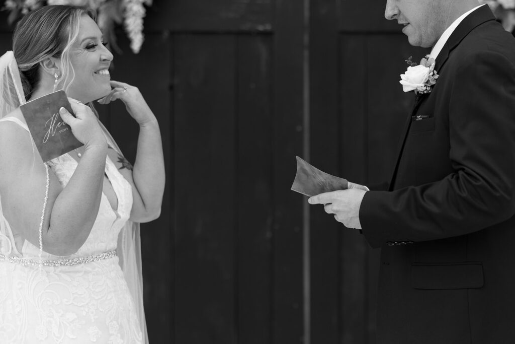 Bride and groom exchanging vows during their first look, with the bride holding a vow booklet and smiling joyfully