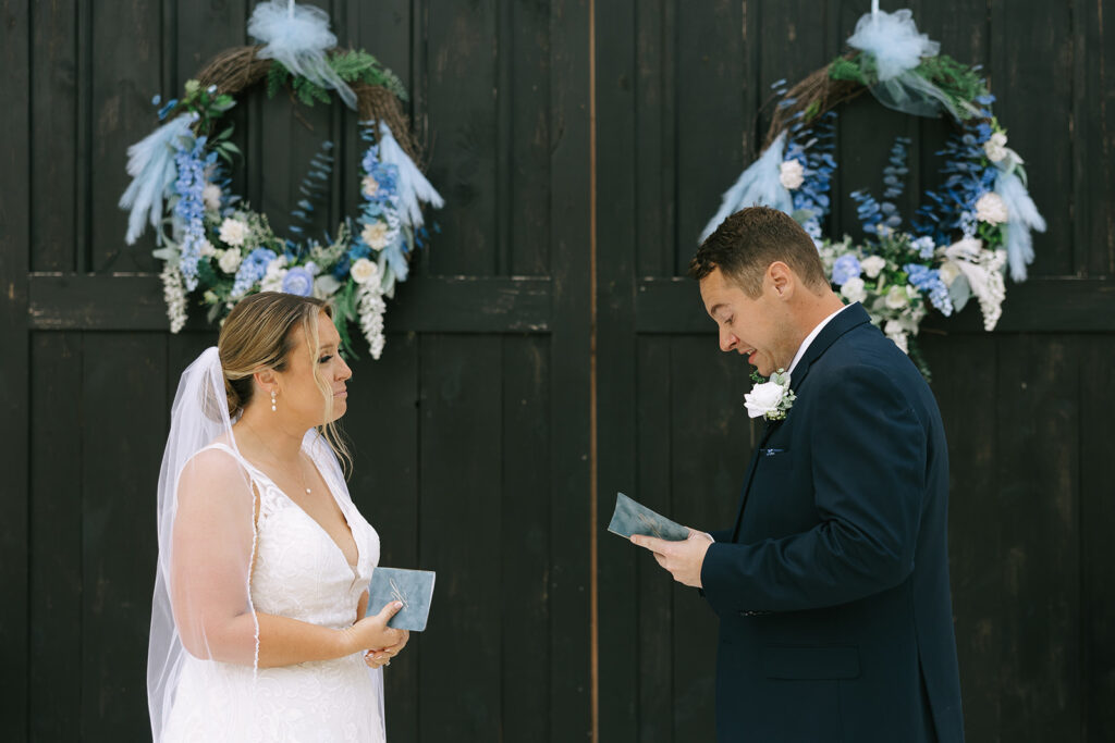 Bride and groom exchanging vows during their first look, with the bride holding a vow booklet and smiling joyfully.