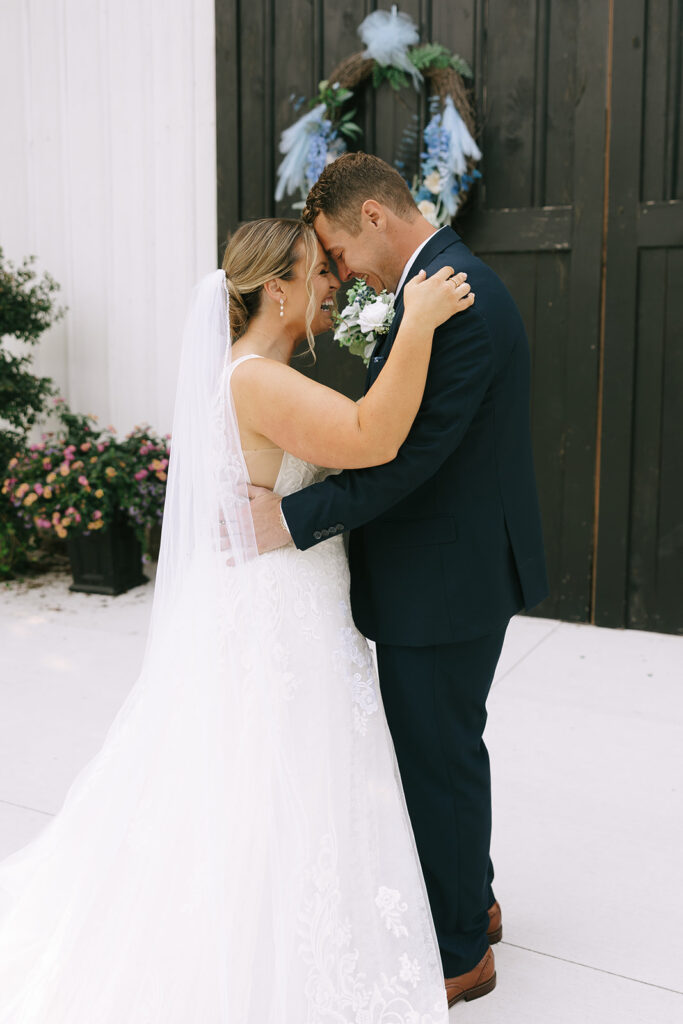 A joyful couple during their first look, embracing and smiling outside a rustic venue, capturing the emotional connection in a First Look vs No First Look moment.