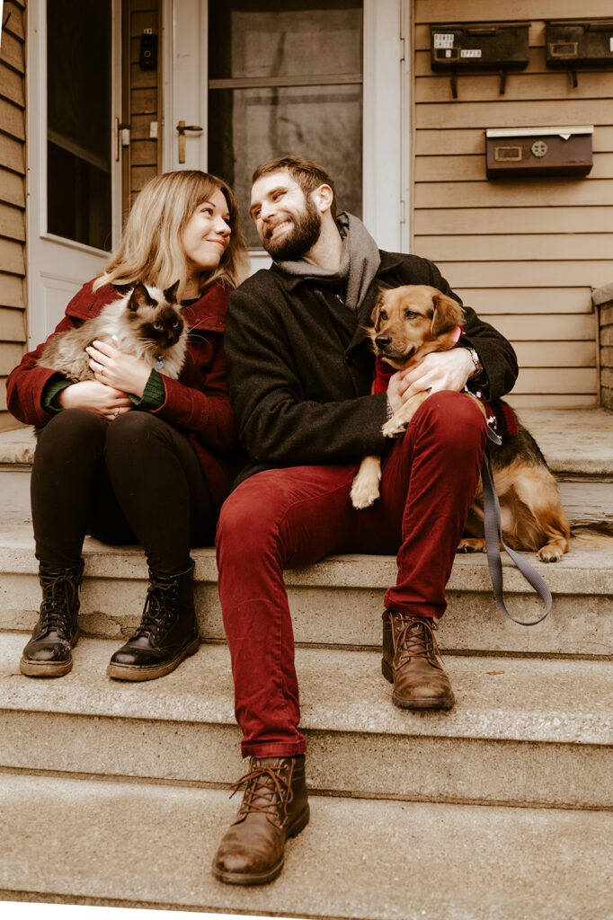 Couple holding their cat while their dog sits nearby, including their dog in engagement photos with their cat
