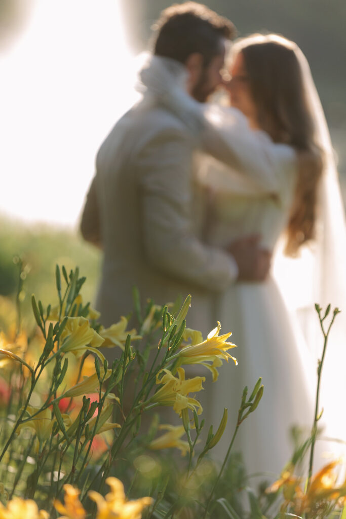  Bride and groom embracing closely in a field of yellow blooms, with golden backlight creating a soft, romantic blur.Blog title of define Your Bridal Look