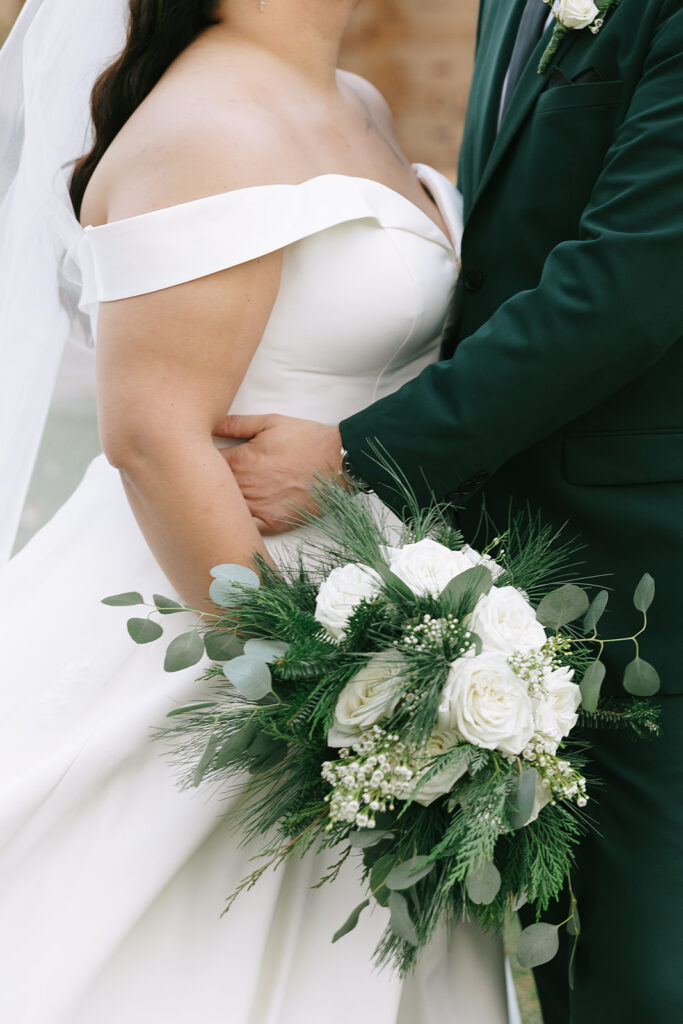 Close-up of bride holding bouquet of white roses while linking arms with the groom, detail shot that matters when finding a wedding photographer on Instagram.