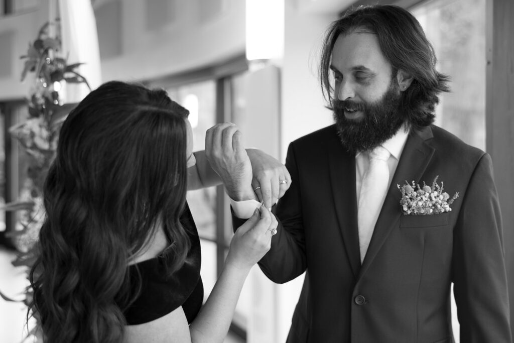 lack and white photo of groom getting cufflinks adjusted, showcasing classic getting-ready moments in tips for the morning of your wedding.