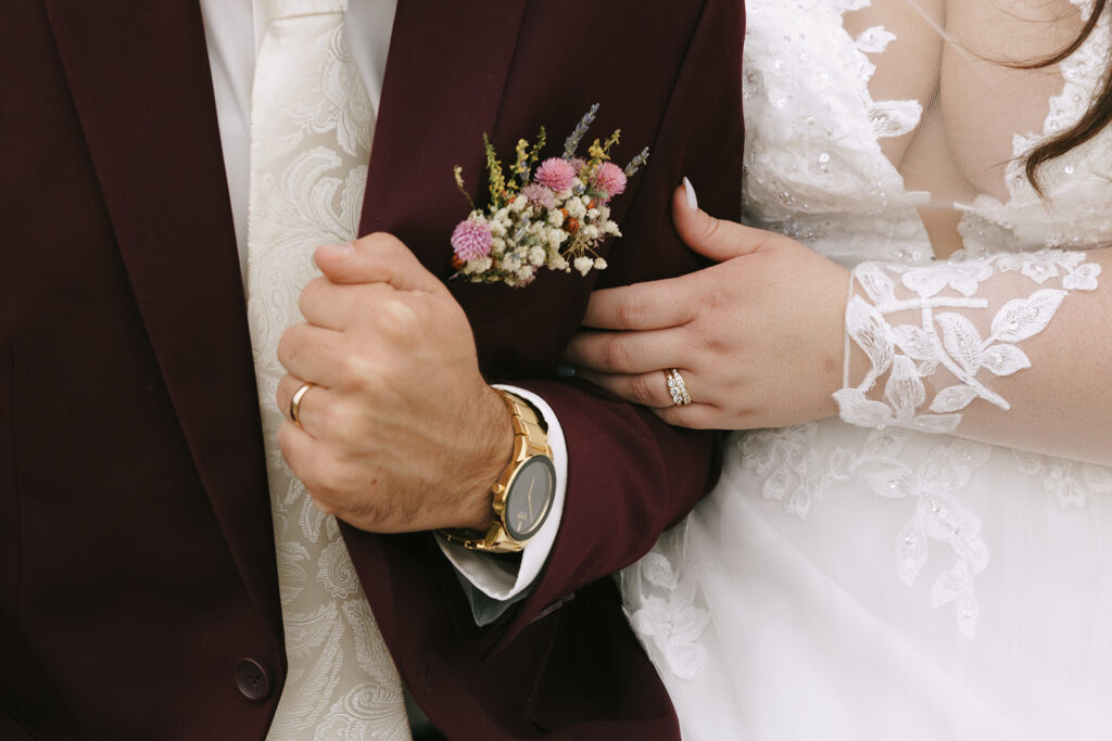 Close-up of bride and groom linking arms, showcasing wedding rings and boutonniere, capturing intimate detail for tips for the morning of your wedding.