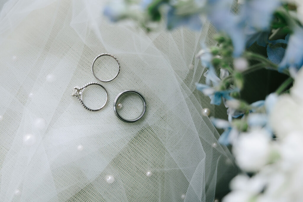 wedding day timeline details with close-up of wedding rings resting on a veil beside soft blue and white florals