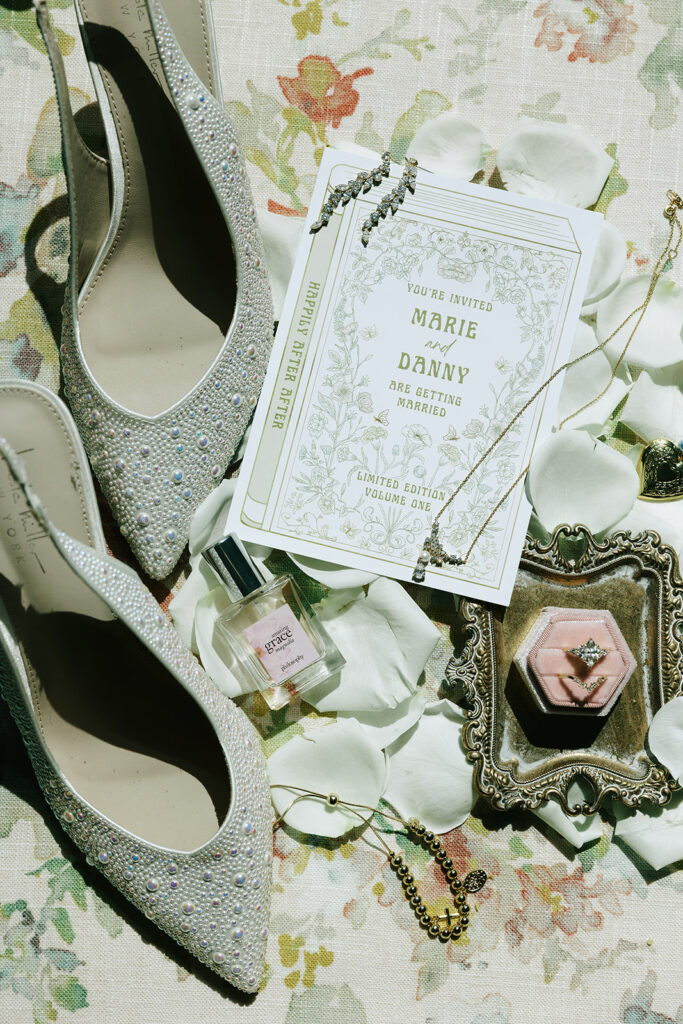 A flat lay of bridal heels, a floral invitation, a white rose, perfume, gold jewelry, and a vintage tray with a pink ring box. Wedding accessories and stationery often purchased during Black Friday wedding deals.

best Black Friday wedding deals