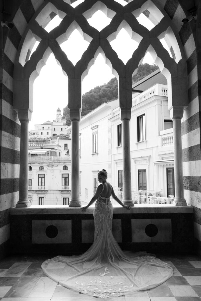 Woman in a wedding dress with her entire dress and train flowing in the photo. The woman is standing in front of an archway.