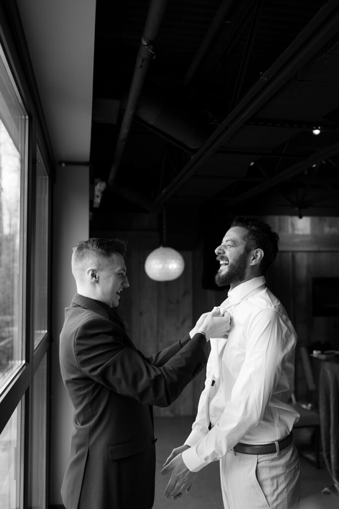 Getting-Ready and Detail Shots of a groom laughing while another man fixes his tie.