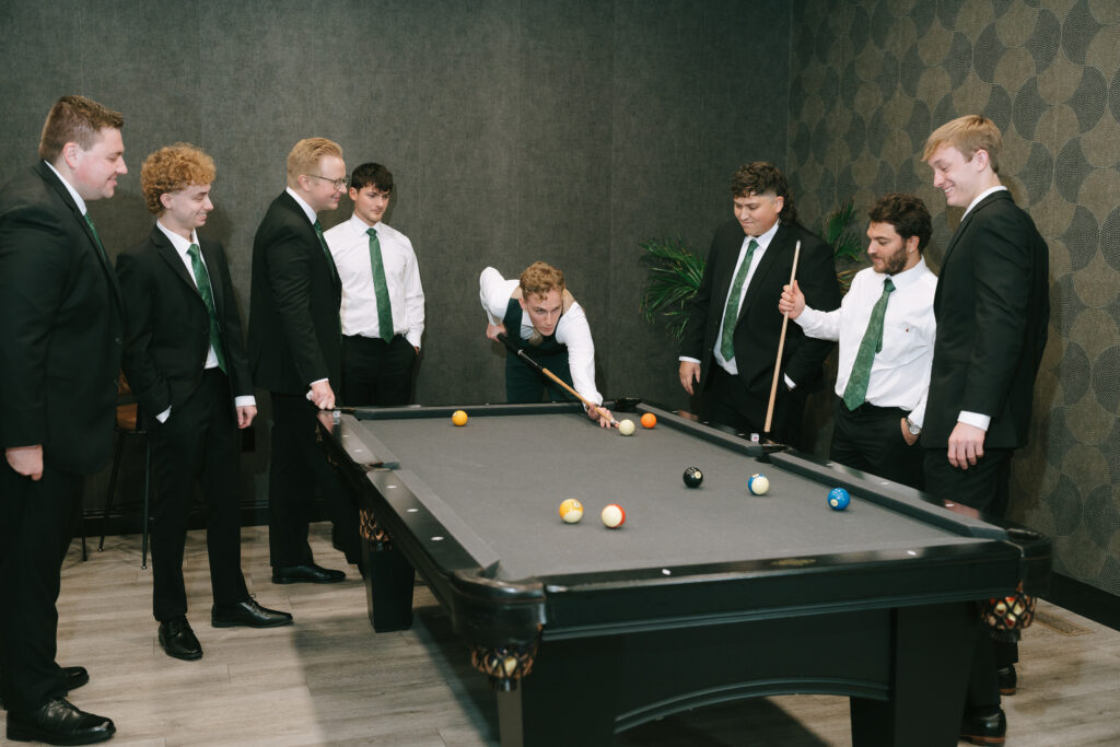 A group of men around a pool table, playing pool indoors as part of their wedding day rain plan.