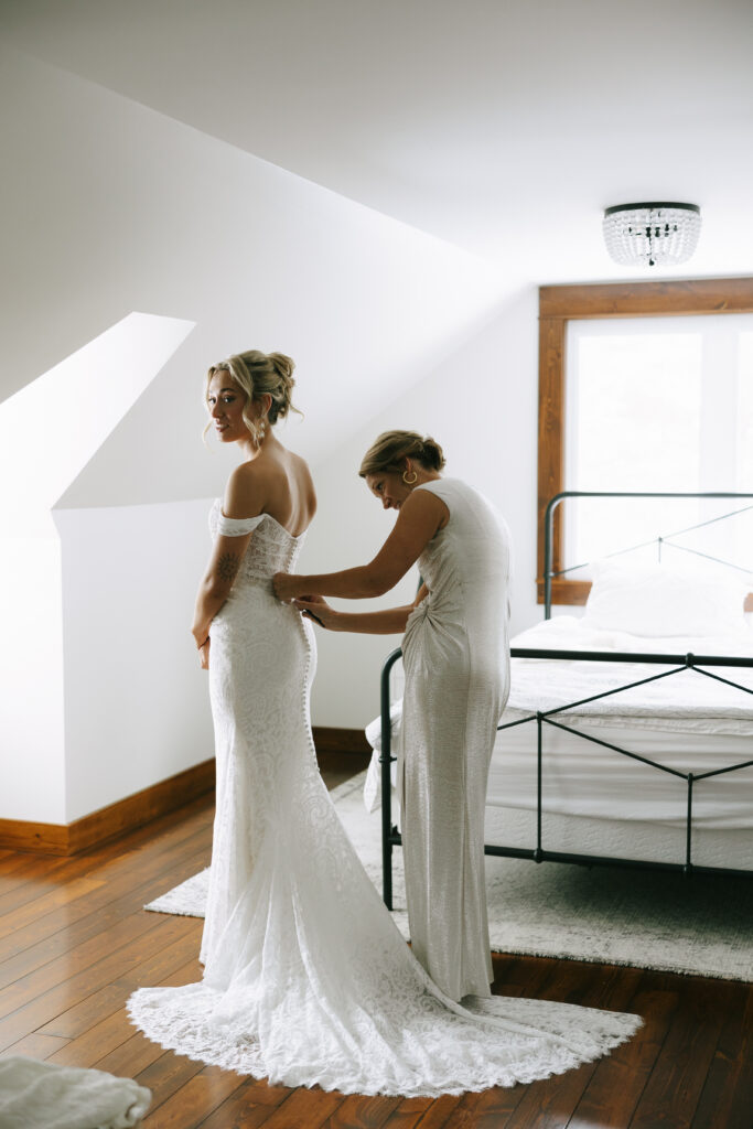Bride getting ready with another woman helping her to get dressed.
