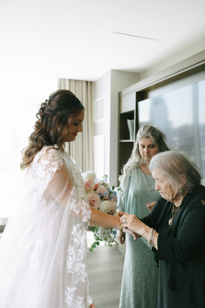 Getting ready photos taken by an Ohio photographer of a woman getting ready. Three women are in the photo, with one woman putting a bracelet on the bride.