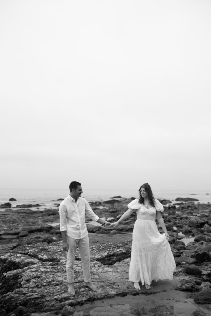 Toledo waterfront wedding portraits featuring the beach with a couple holding hands on the rocks.