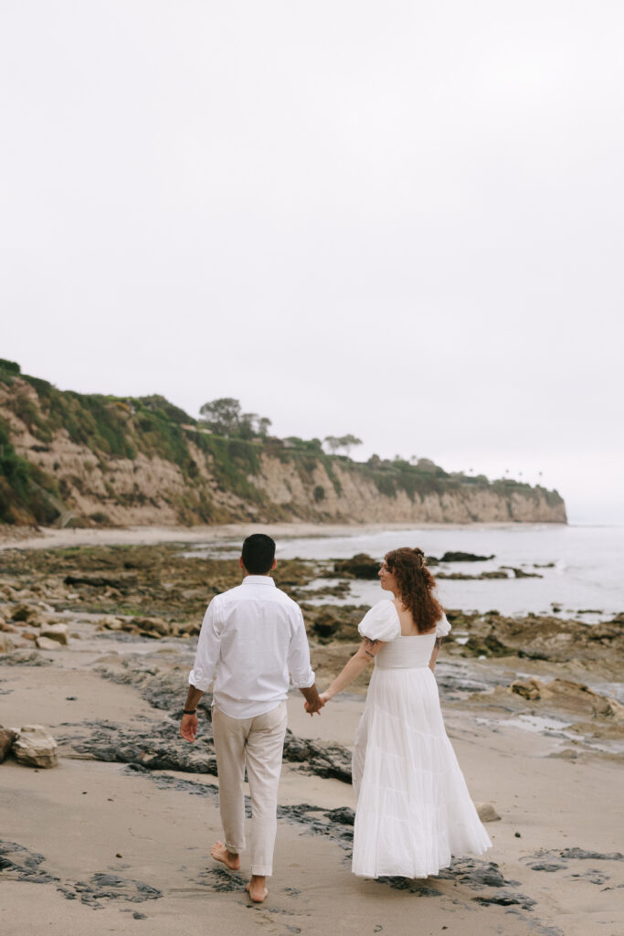 Toledo waterfront wedding portraits featuring the beach with a couple holding hands and walking. 