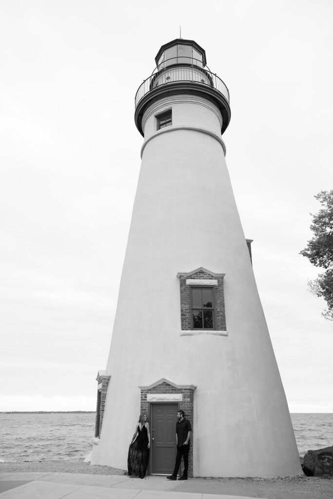 Black and white image with a woman and man on the beach at a lighthouse.