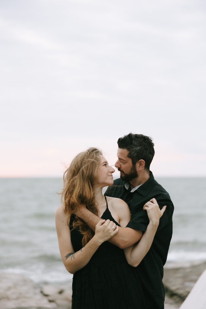 Woman and man on the beach smiling and holding each other while the photographer gives advice for engaged couples.