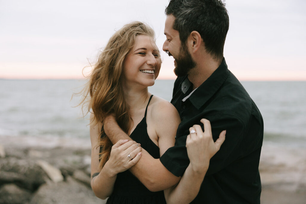 Woman and man on the beach smiling at each other while the photographer gives advice for engaged couples.