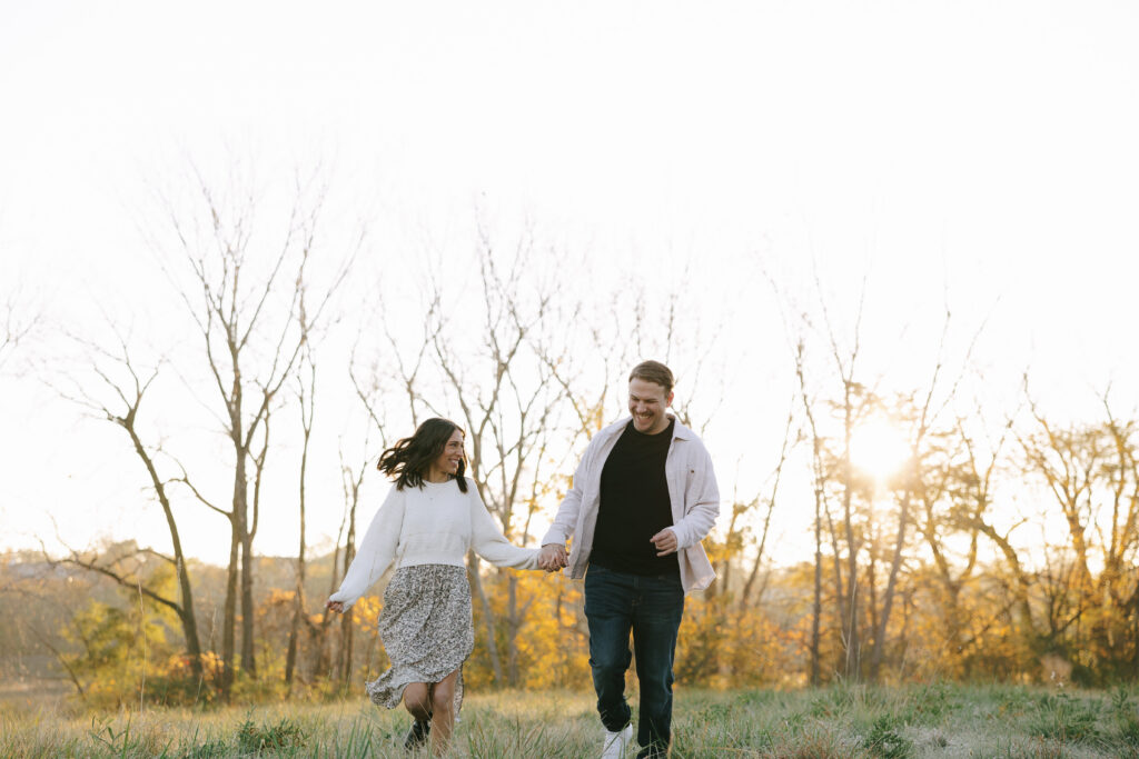 Couple laughing, holding hands in the grass together during their engagement photos for camera-shy couples.