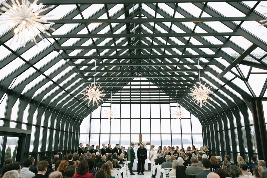 Wedding ceremony inside a glass conservatory venue with dramatic starburst chandeliers, Toledo wedding photographer