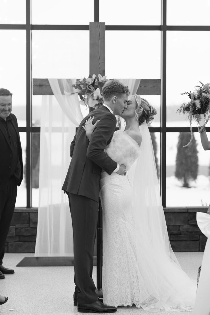 Bride and groom embracing in front of large windows, black and white wedding portrait