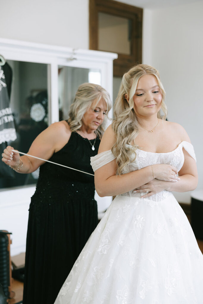 Mother helping bride lace up wedding dress in candid photograph
