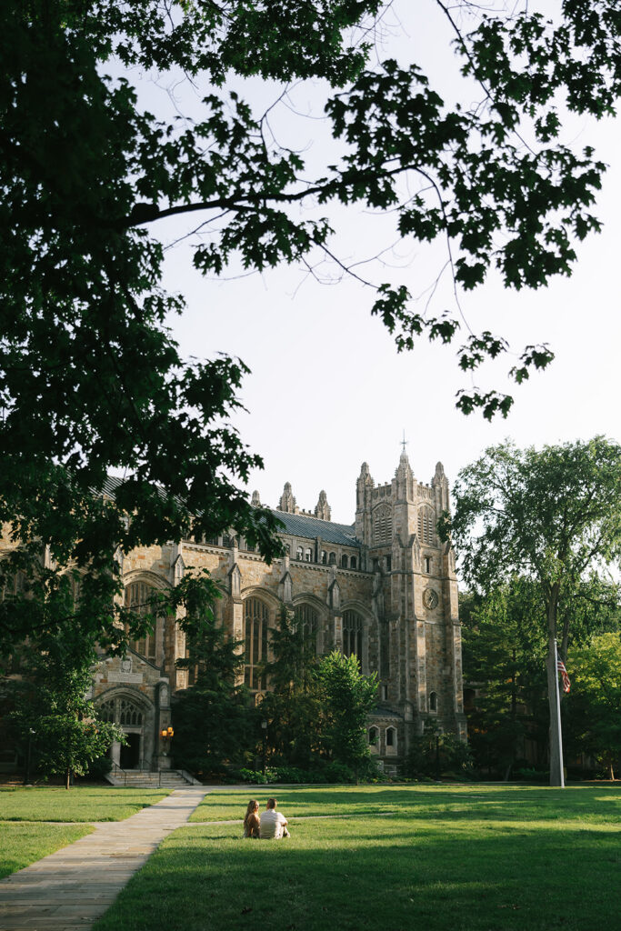 Engaged couple walking across a grassy lawn near a historic building
